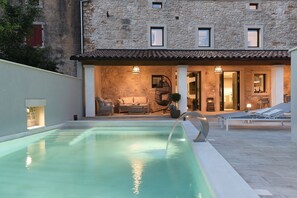 A swimming pool with a stone building in the background, a patio area with lounge chairs, and a stone wall.