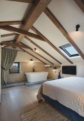 A bedroom with a skylight, a large bed, a bathtub, and a TV.