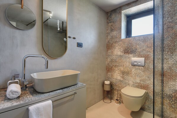 A bathroom with a large oval sink, a mirror, a toilet, and a shower area with a textured wall.