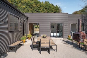 Un patio esterno moderno con tavolo e sedie in legno, una griglia per barbecue e piante in vaso.