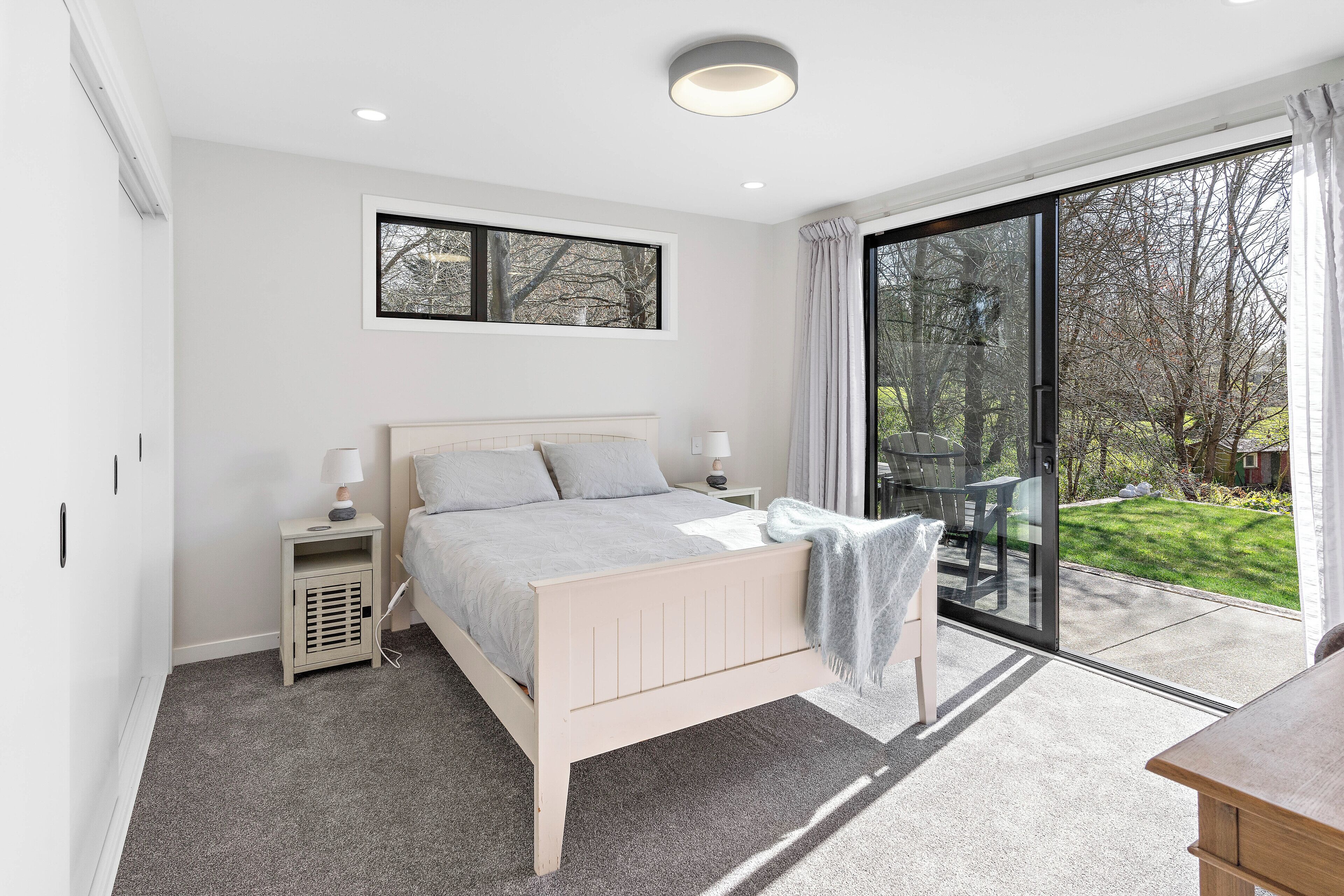 Ein Schlafzimmer mit Bett, Nachttischen, einem Fenster und Blick auf einen Garten.