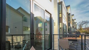 Un edificio moderno con grandes puertas y ventanas de vidrio, una terraza de madera con sillas y una barandilla metálica.