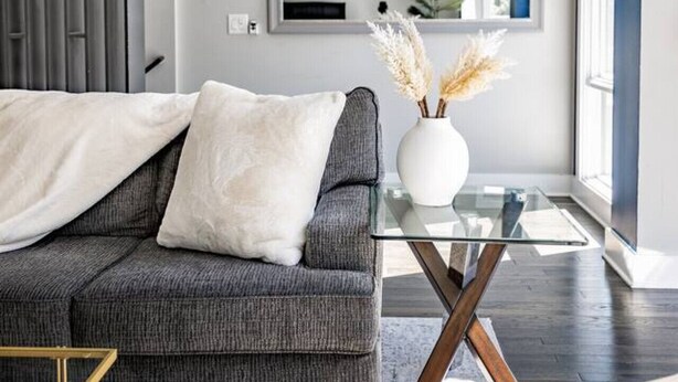 Una sala de estar moderna con un sofá gris, una mesa de centro de vidrio y un jarrón decorativo con plantas secas.