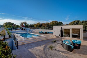 Et moderne poolområde med en lille legeplads, siddepladser og en tilbygning med glasfacade.