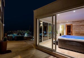 Een modern terras buiten met een jacuzzi, een zithoek en een glazen deur die naar een kamer leidt.