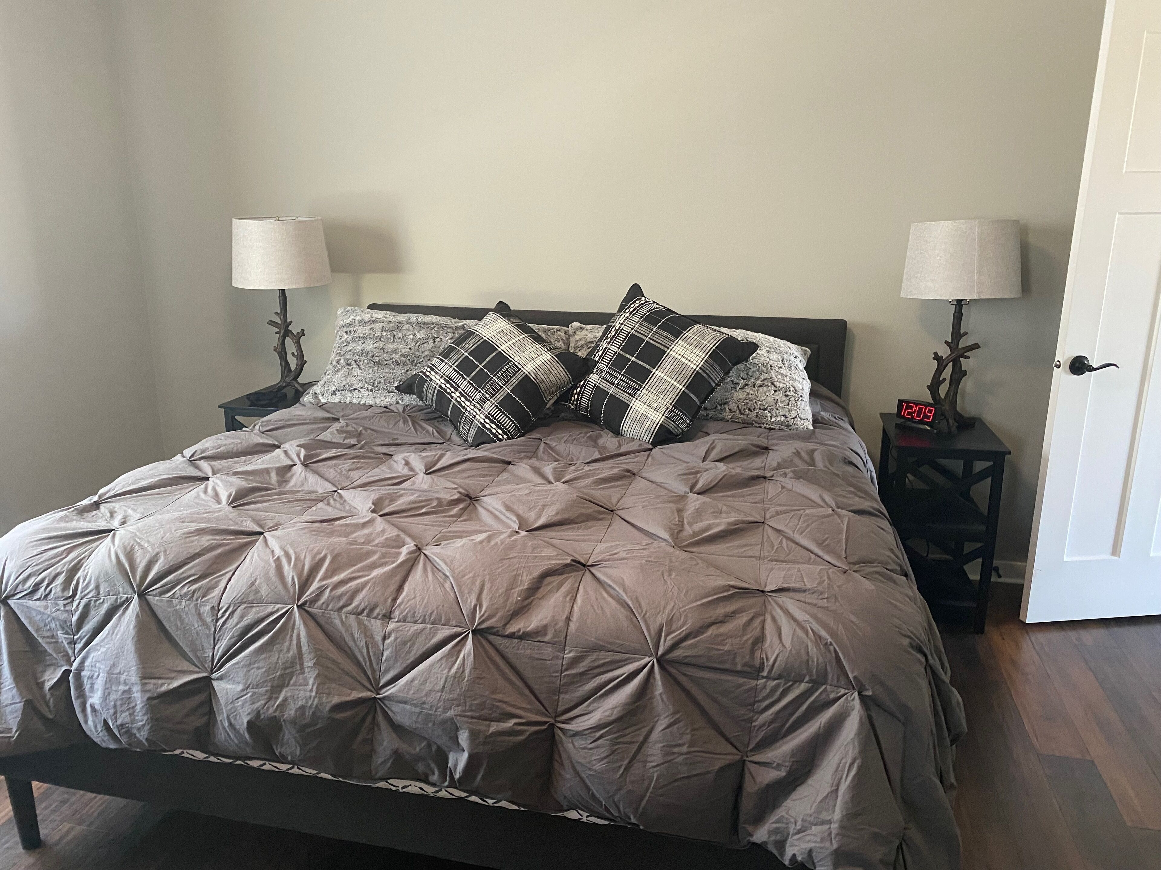 Una cama bien tendida con una colcha marrón y dos almohadones decorativos, flanqueada por dos mesitas de noche con lámparas.