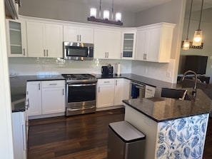 A modern kitchen with white cabinets, stainless steel appliances, and a wooden floor.