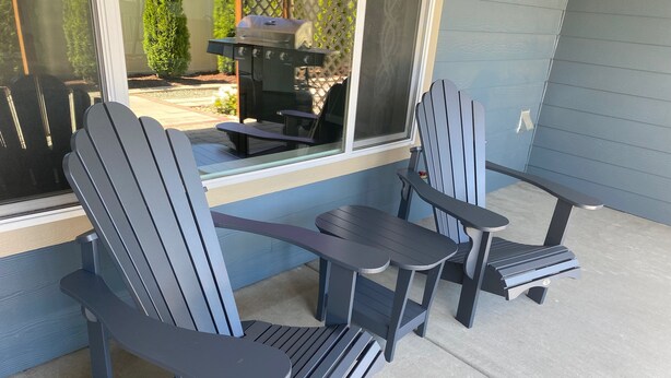 Eine Veranda mit Adirondack-Stühlen, einem kleinen Tisch, einem Grill und Blick auf den Garten.