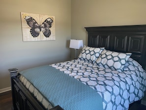 A bedroom with a bed, a headboard, a wall-mounted lamp, and a butterfly artwork.