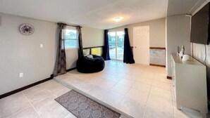 A spacious living area with a large window, a clock on the wall, and a sliding door leading to an outdoor area. - DIRECT Gulf View/Access! KAYAKS!!! WATERFRONT!!! (Hernando Beach)