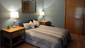Une chambre à coucher avec un lit, deux tables de chevet, un miroir, une porte en bois et une petite table de nuit sur laquelle est posée une plante.