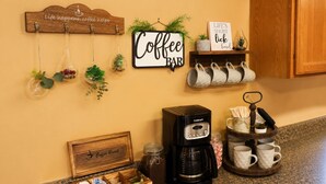 A kitchen counter with a coffee maker, mugs, a coffee bar sign, and a coffee break sign.