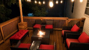 Une terrasse extérieure aménagée avec des meubles en osier, des coussins rouges et un foyer.