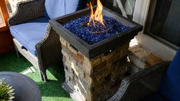 Ein Feuerkorb aus Stein mit blauer Glasoberfläche, umgeben von Korbmöbeln.