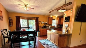 Une cuisine spacieuse avec des meubles en bois, un coin repas comprenant une table et des chaises, et un ventilateur de plafond.