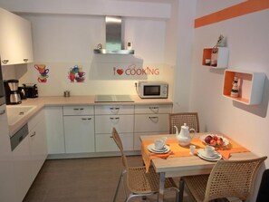 A compact kitchen with white cabinets, a microwave, and a coffee maker. A dining table with chairs is set up in the center.