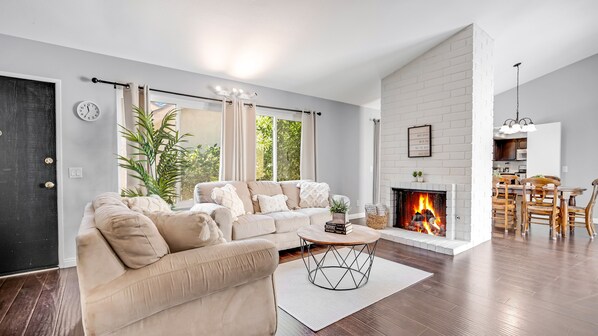 A modern living room with a sectional sofa, a fireplace, and a dining area with wooden chairs.