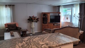 Uma sala de estar com bancada de mármore, armários de madeira, televisão e janela com cortinas.