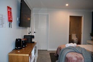 A bedroom with a bed, bedside table, TV, and a door leading to a bathroom. - Contemporary B&B with Ensuite, Kitchenette and Separate Entrance (Aylmerton)