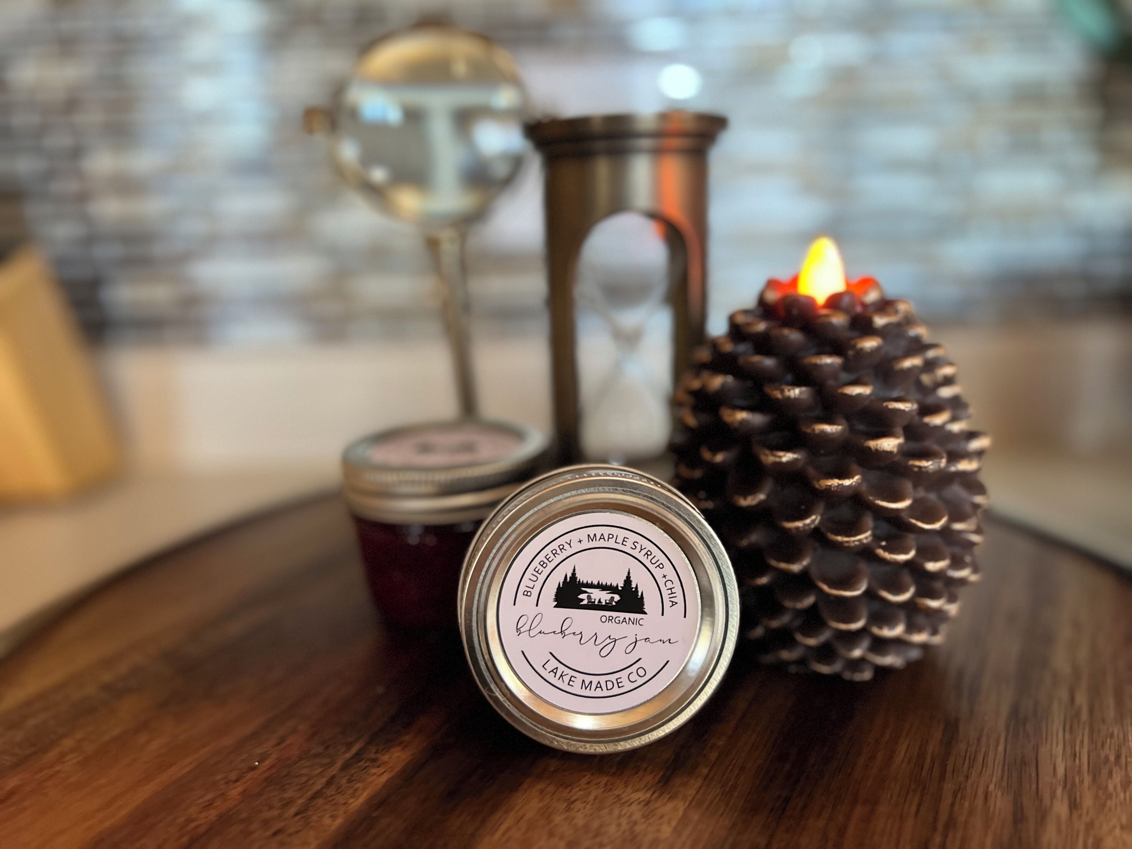 A wooden table with a candle, a pine cone, and two jars.