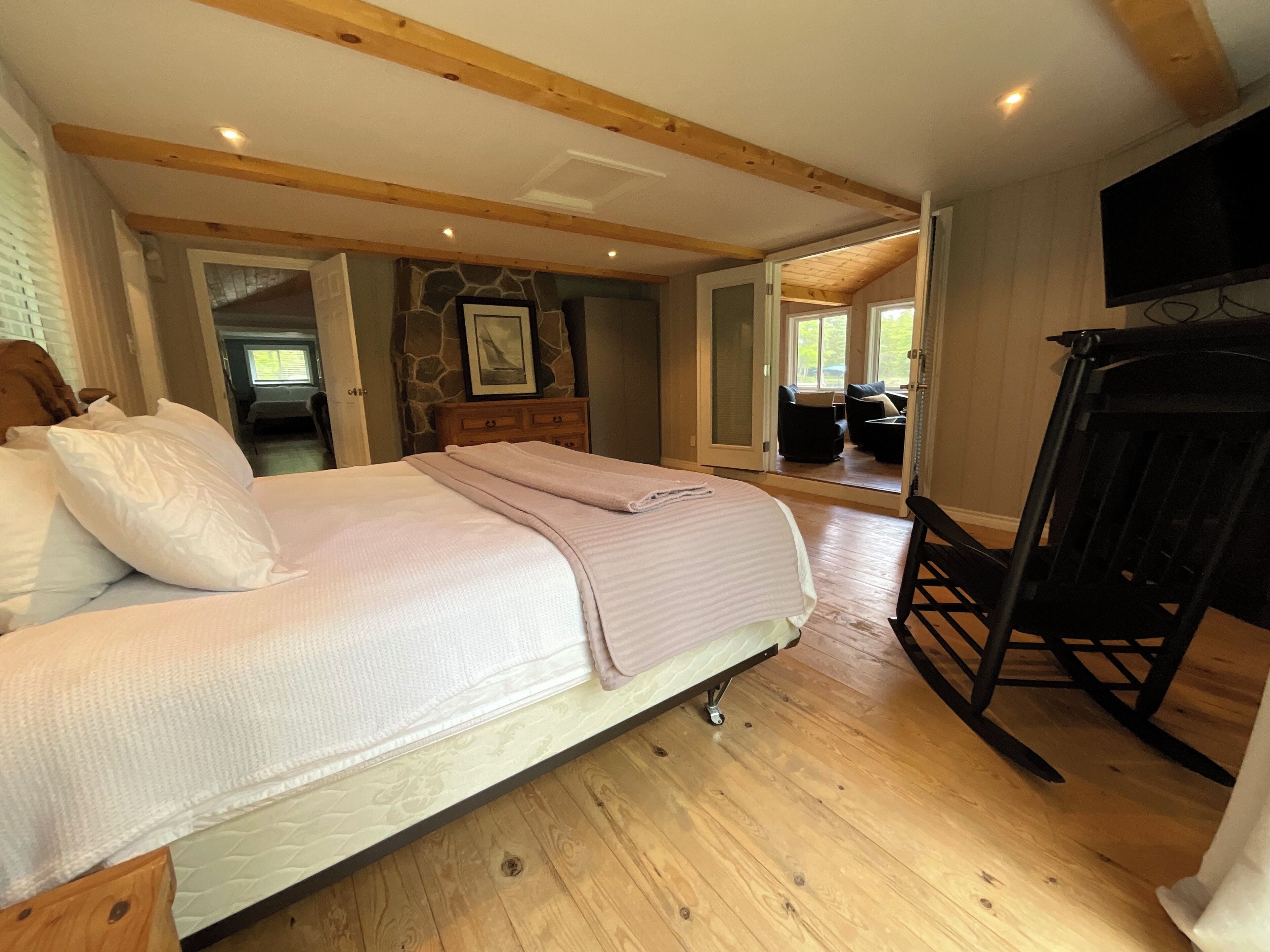Une chambre à coucher avec un lit, un plancher en bois, un mur en pierre, une télévision et une vue sur l’extérieur.
