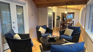 A cozy interior with wicker furniture, a central coffee table, and a view into the kitchen area. - Bright and spacious lakeside cottage with firepit, hot tub and AC on Stoney Lake (Lakefield)