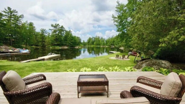 A deck with wicker furniture and a view of a lake. - Bright and spacious lakeside cottage with firepit, hot tub and AC on Stoney Lake (Lakefield)