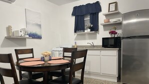 Une cuisine compacte avec des meubles blancs, un réfrigérateur en acier inoxydable, un four à micro-ondes et une cuisinière. On y trouve une table à manger avec quatre chaises et un vase de fleurs.