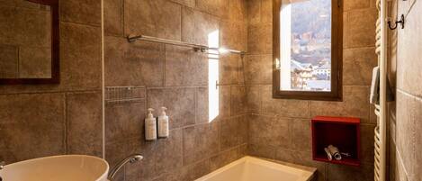 Un baño con una bañera grande, un lavabo y una ventana que ofrece vistas a un paisaje nevado.