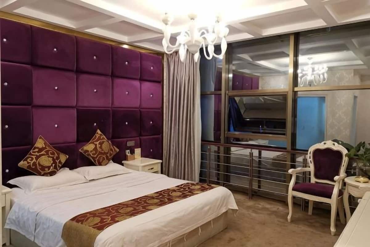Hotellihuone, jossa on suuri sänky, kattokruunu, näköalalla varustettu ikkuna ja tuoli.