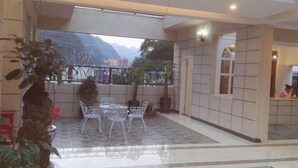Un espacio interior amplio con suelo de baldosas, una zona de estar con sillas blancas y vistas a montañas a través de un gran ventanal.