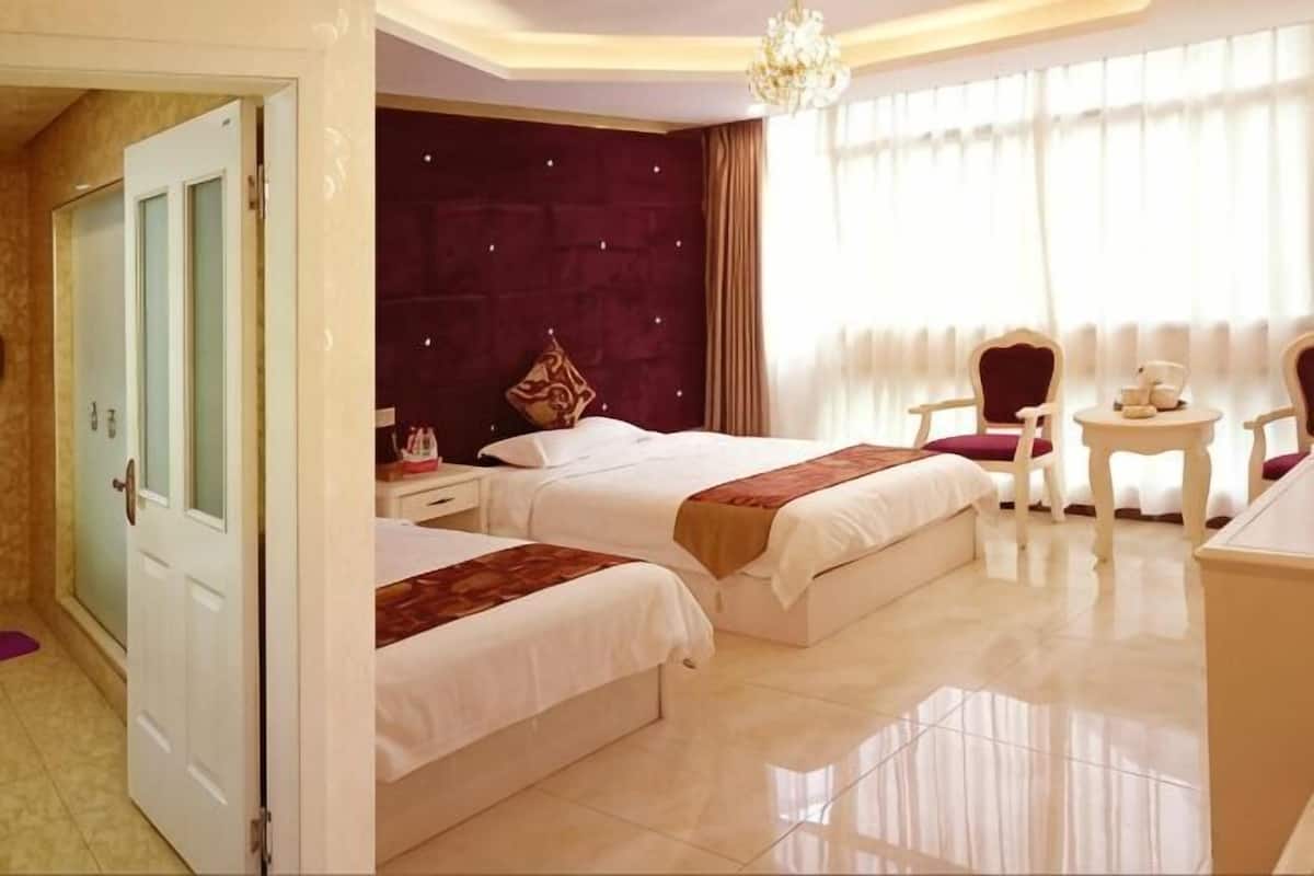 A hotel room with two beds, a sitting area with a table and chairs, a chandelier, and a large window with curtains.