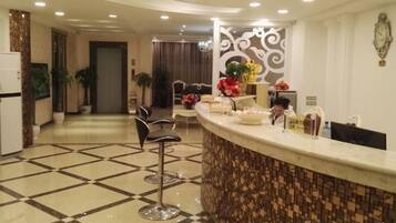 A hotel lobby with a reception desk, bar stools, a patterned floor, and a decorative wall.