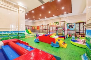 Un espace de jeux intérieur avec des toboggans, des structures de jeu et une moquette verte.