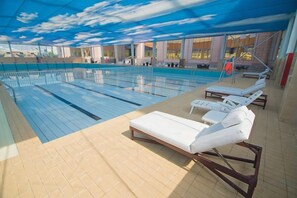 Una piscina interior con varias pistas, tumbonas y una zona cubierta.