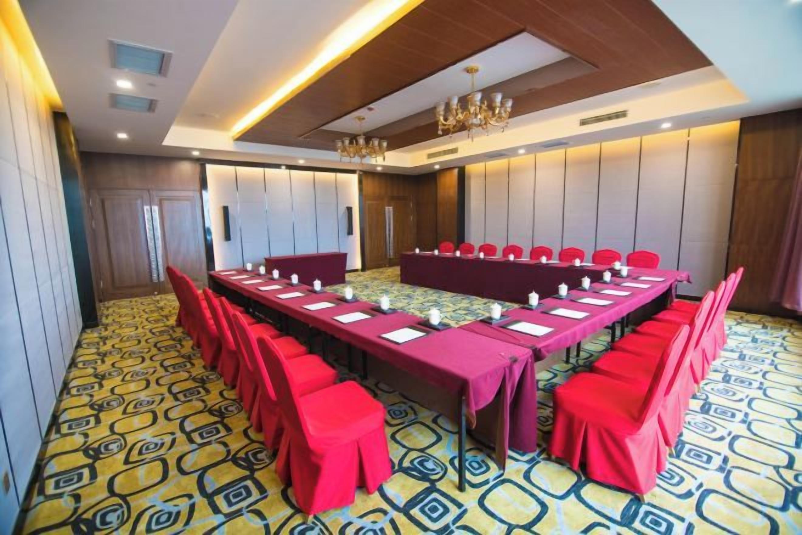 A conference room with a long table, red chairs, and a patterned carpet.
