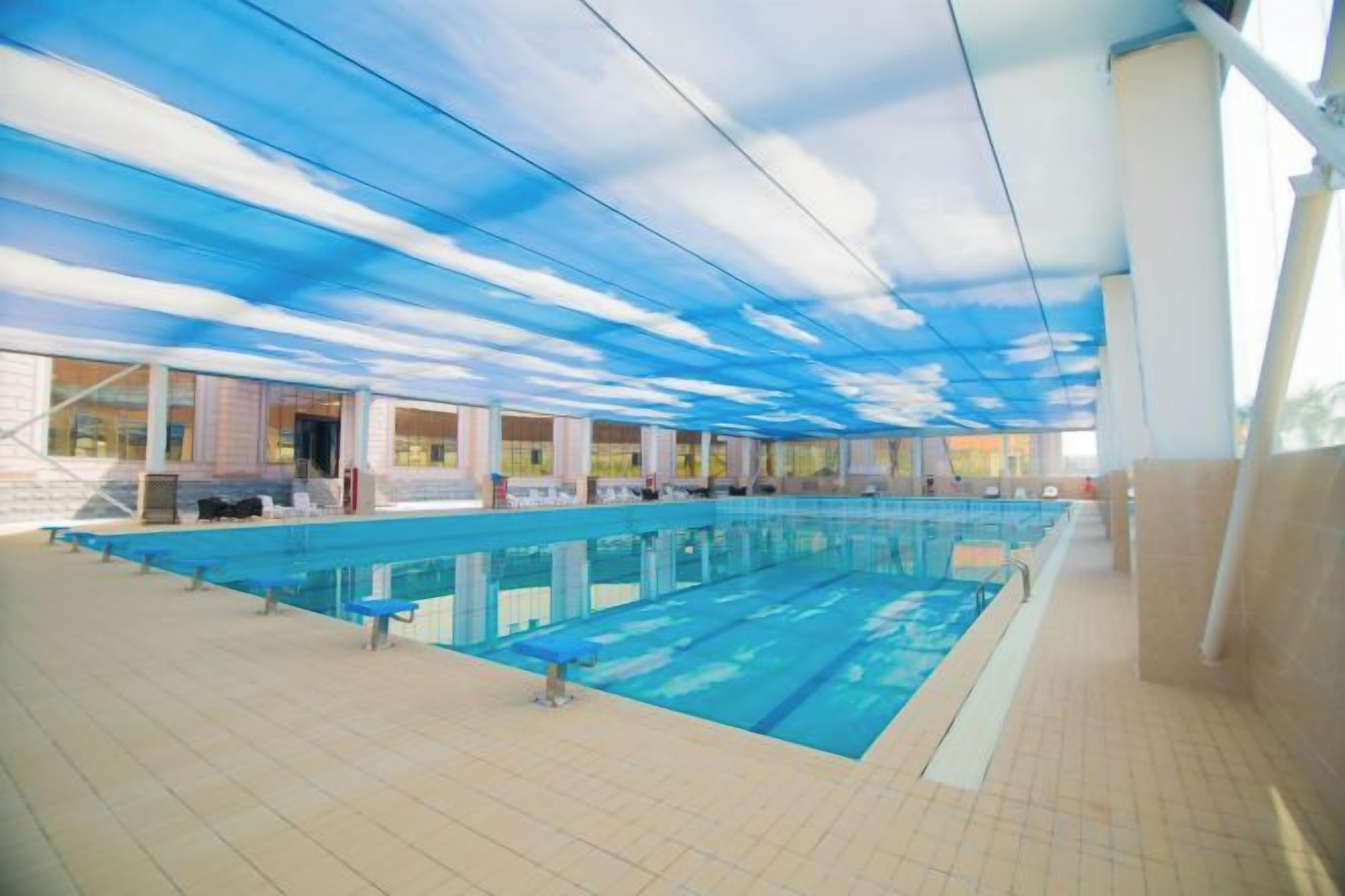 Una piscina coperta con diverse corsie, pavimento piastrellato e soffitto decorato con un motivo nuvoloso.