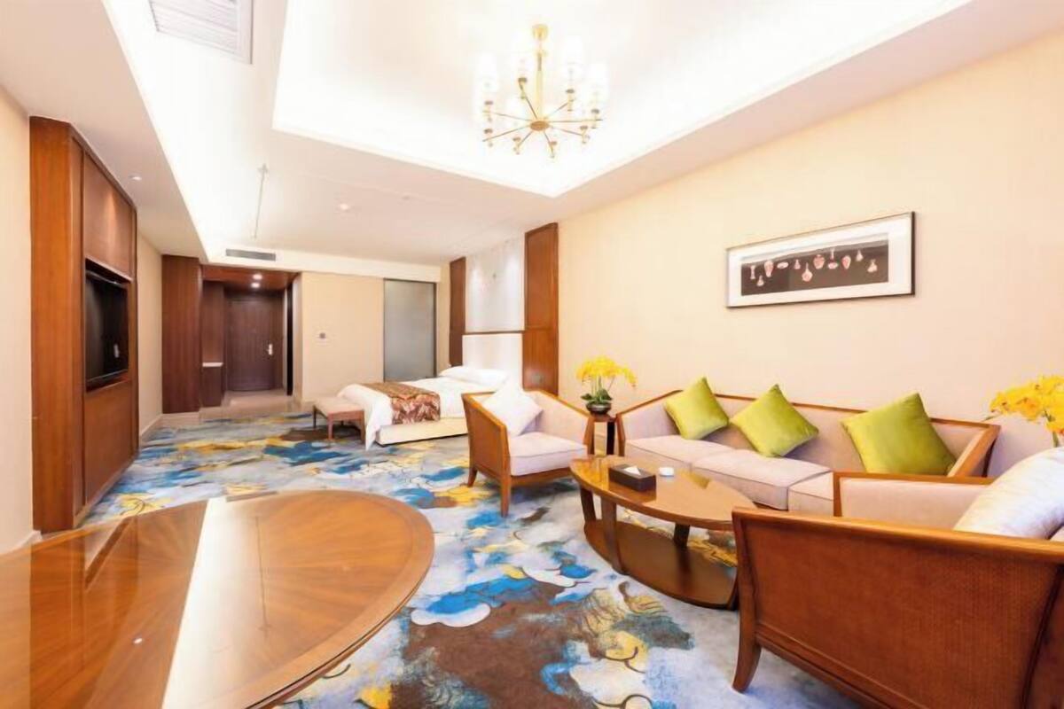 A hotel lobby with a large wooden coffee table, a sofa set, a chandelier, and a framed artwork on the wall.