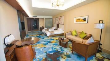 A hotel room with a large bed, a sofa, a desk with a chair, and a chandelier.