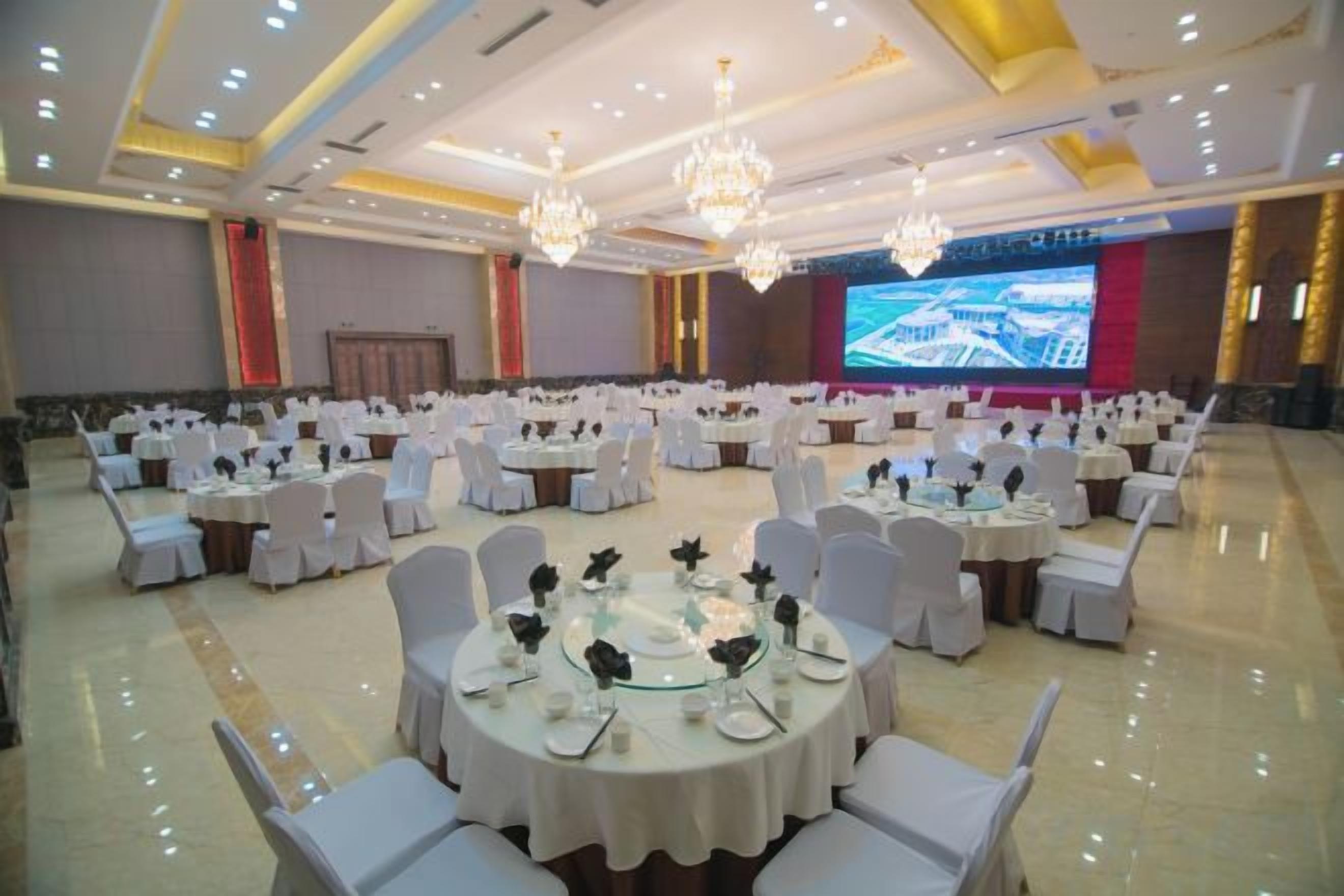 A banquet hall with round tables and chairs, a large screen, and chandeliers.