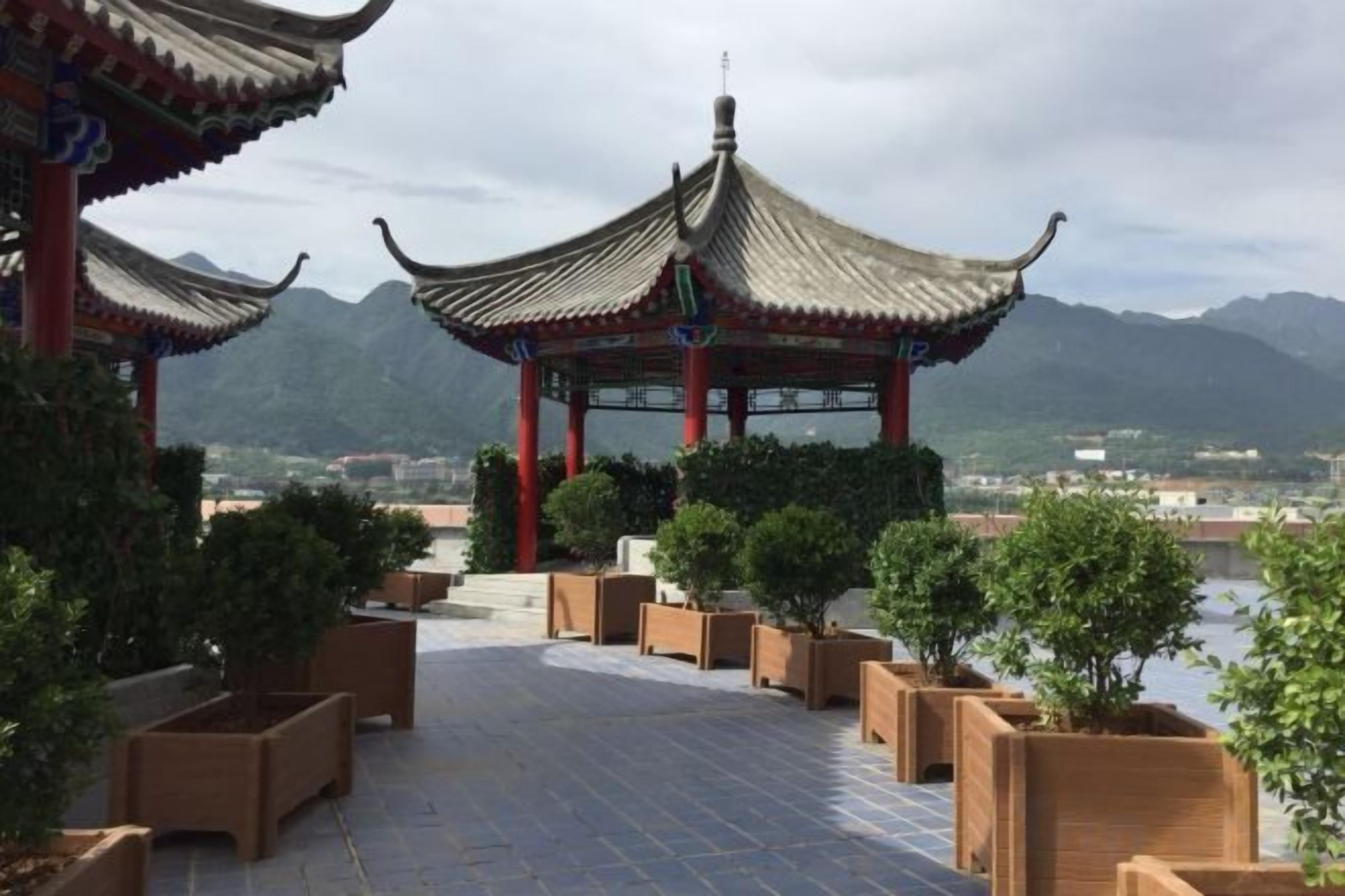 A traditional Chinese pavilion with a tiled walkway leading to it, surrounded by potted plants.