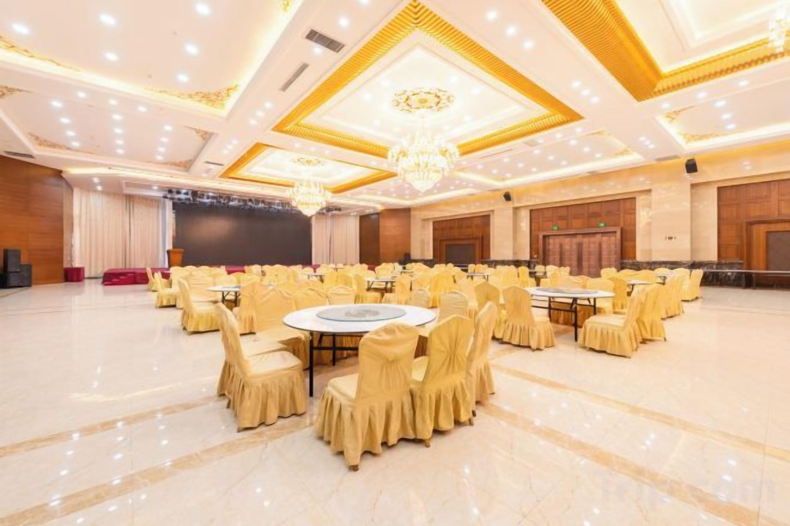 A banquet hall with round tables and chairs, a stage, and a chandelier.