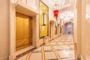Un pasillo de hotel con piso de diseño ajedrezado, una puerta dorada y un adorno rojo.