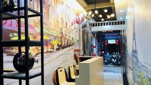 Zona de recepción con un mural de una escena callejera, mostrador de recepción y sillones.