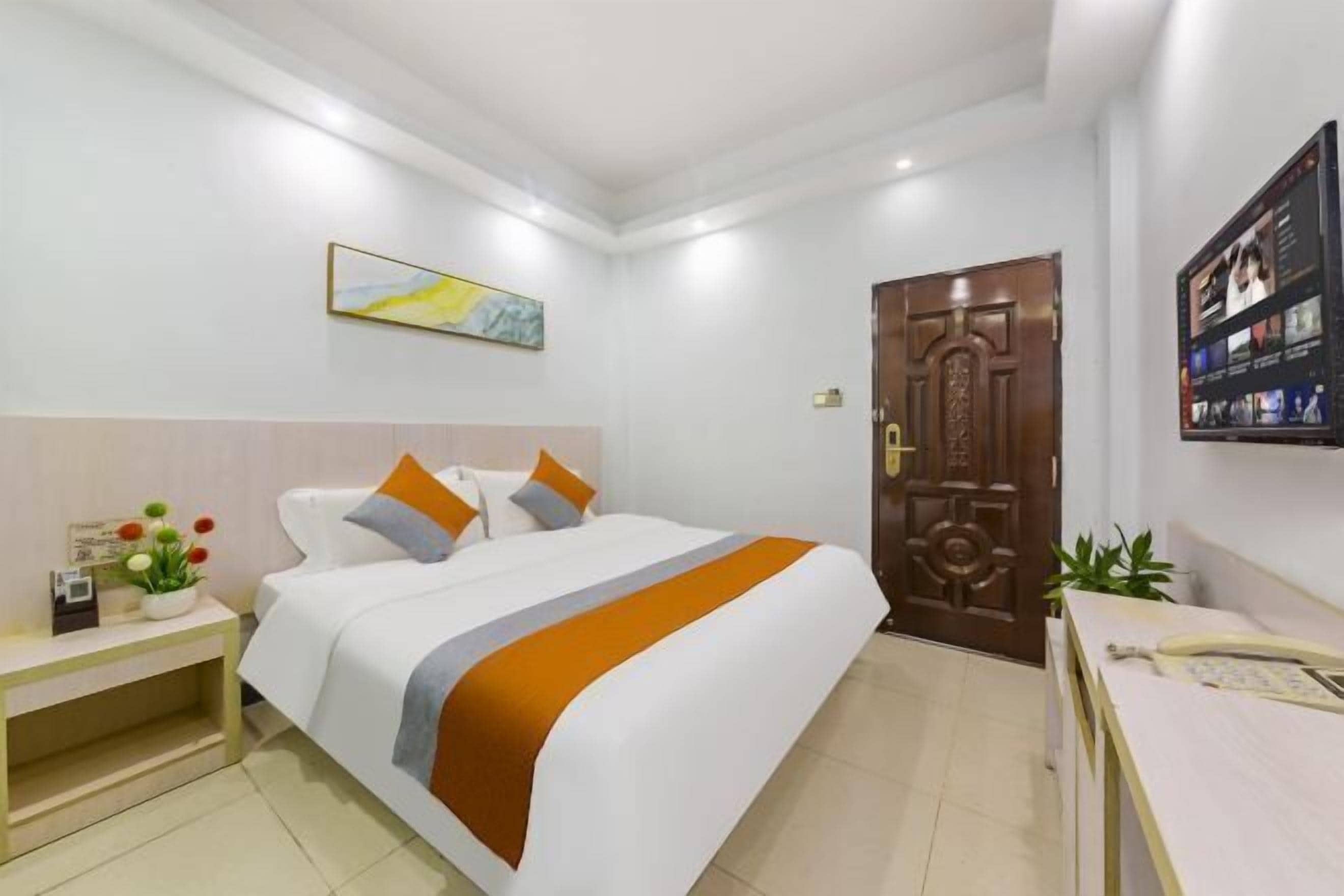 A hotel room with a bed, a nightstand, a desk, a door, and a wall-mounted TV.