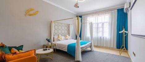 A bedroom with a four-poster bed, a small bedside table, a chair, and a sofa.