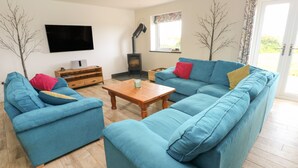 A living room with a blue sofa set, a wooden coffee table, a flat-screen TV mounted on the wall, and a fireplace. - Landfall (Pembroke)
