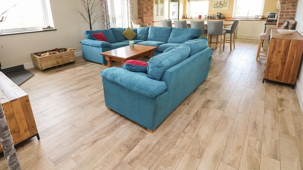 A spacious living room with a large blue sectional sofa, a wooden coffee table, and a kitchen area visible in the background. - Landfall (Pembroke)