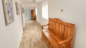 A hallway with a wooden bench, framed artwork on the walls, and a door at the end. - Landfall (Pembroke)