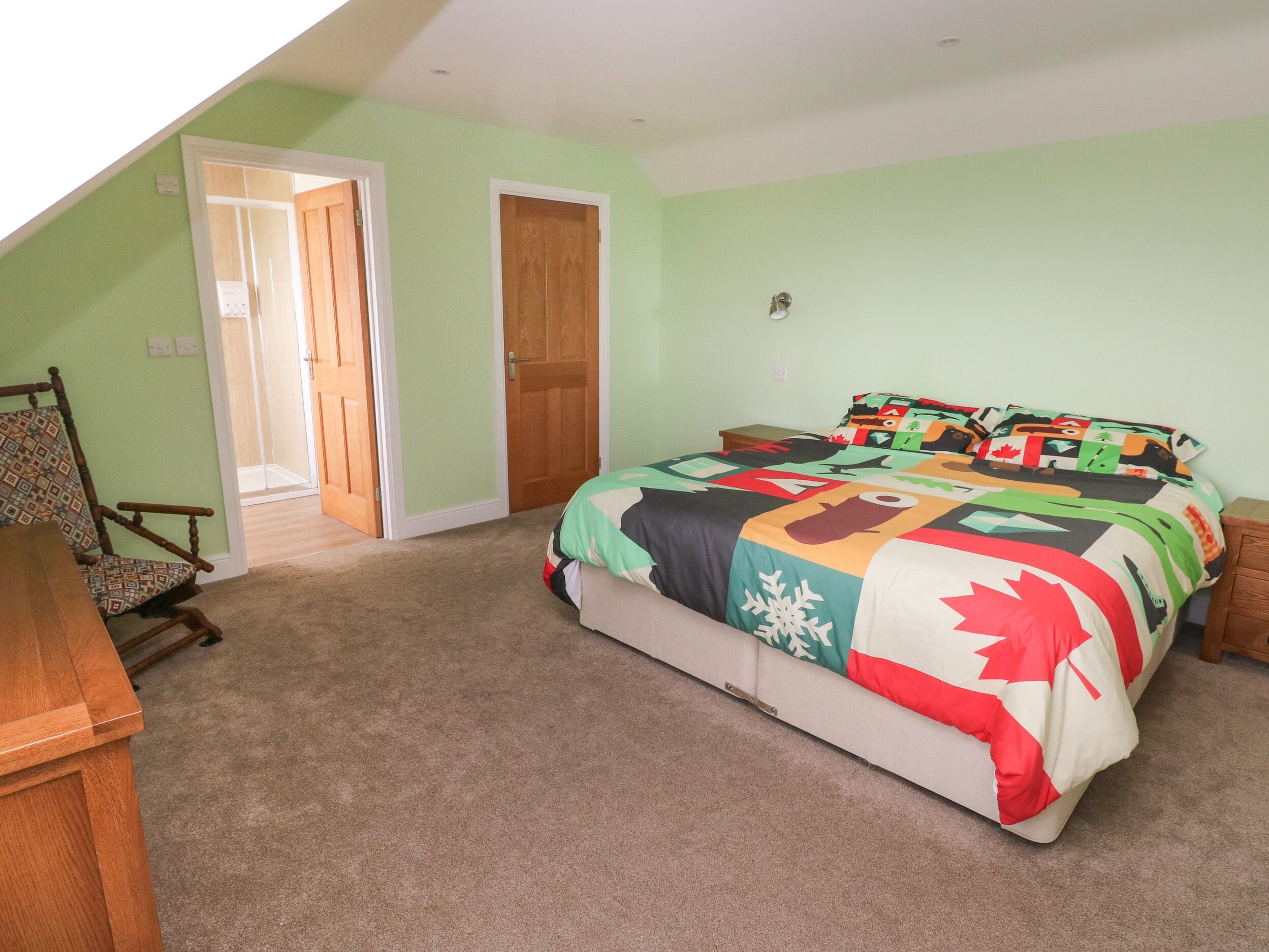 Une chambre à coucher comprenant un lit, une chaise, une table de chevet en bois et une porte donnant sur une autre pièce.
